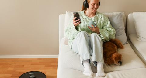 Nainen puhelimella sohvalla, robottipölynimuri lattialla