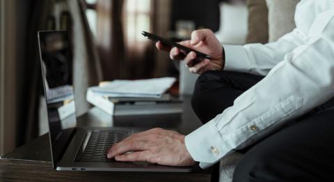 mies käyttämässä tietokonetta ja puhelinta